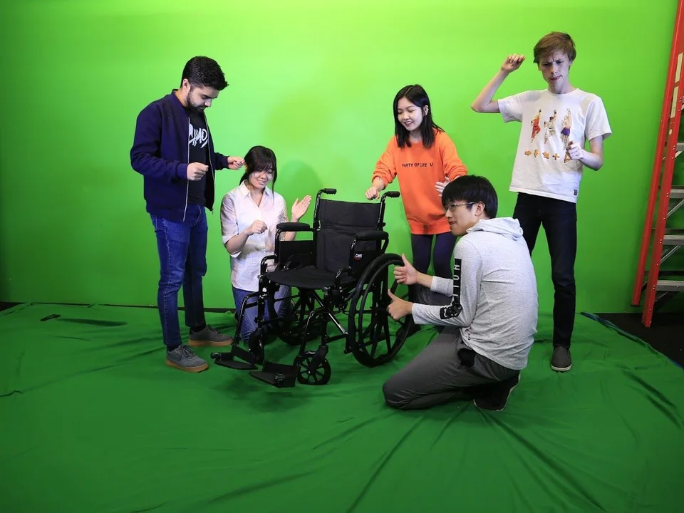 Classmates gathered around a wheelchair in a green-screen studio