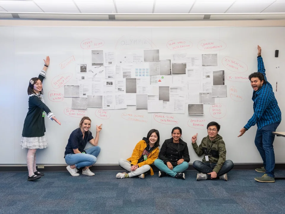 A project team posing in front of a whiteboard of game ideas