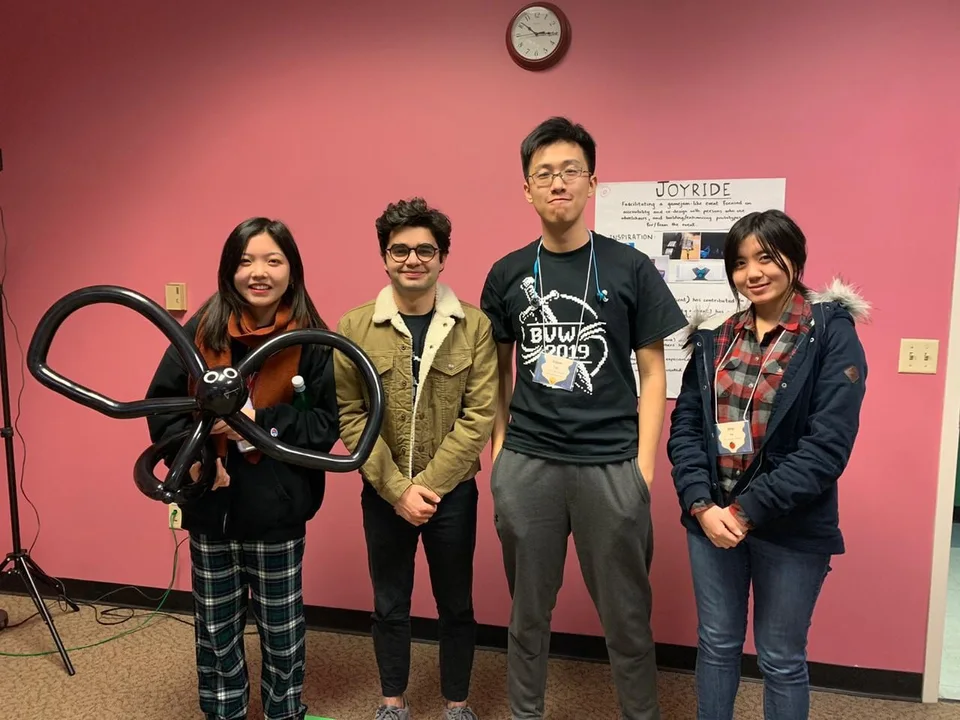 Four friends at a project showcase, one holding a balloon creature